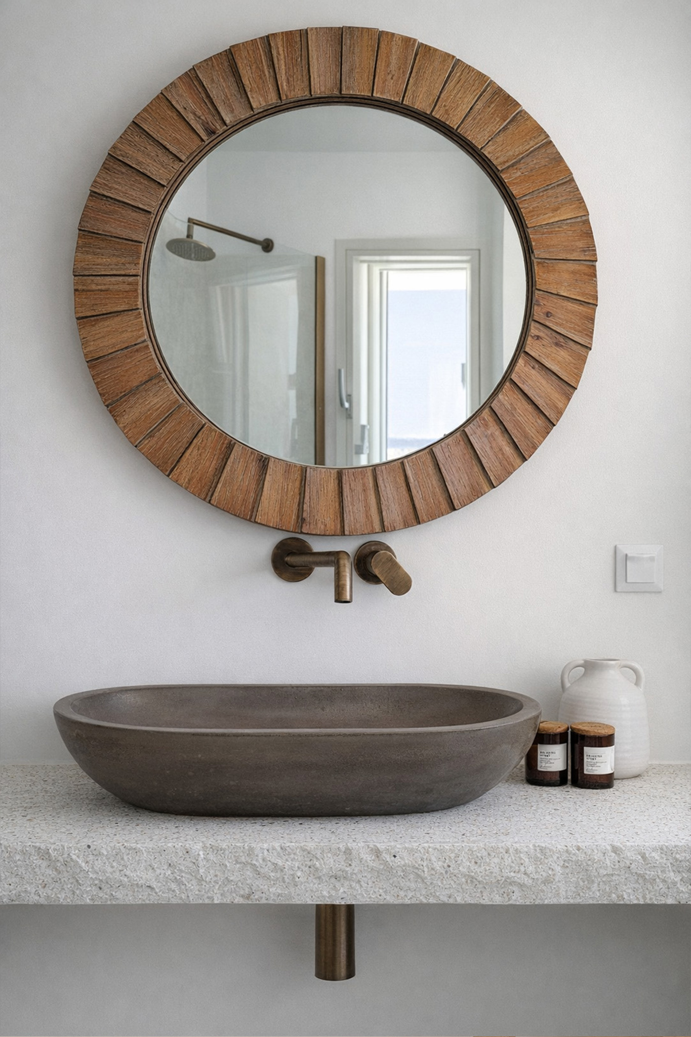 Bathroom vanity in an Andros Cycladic residence with stone basin, round wood mirror and bronze wall-mounted faucet