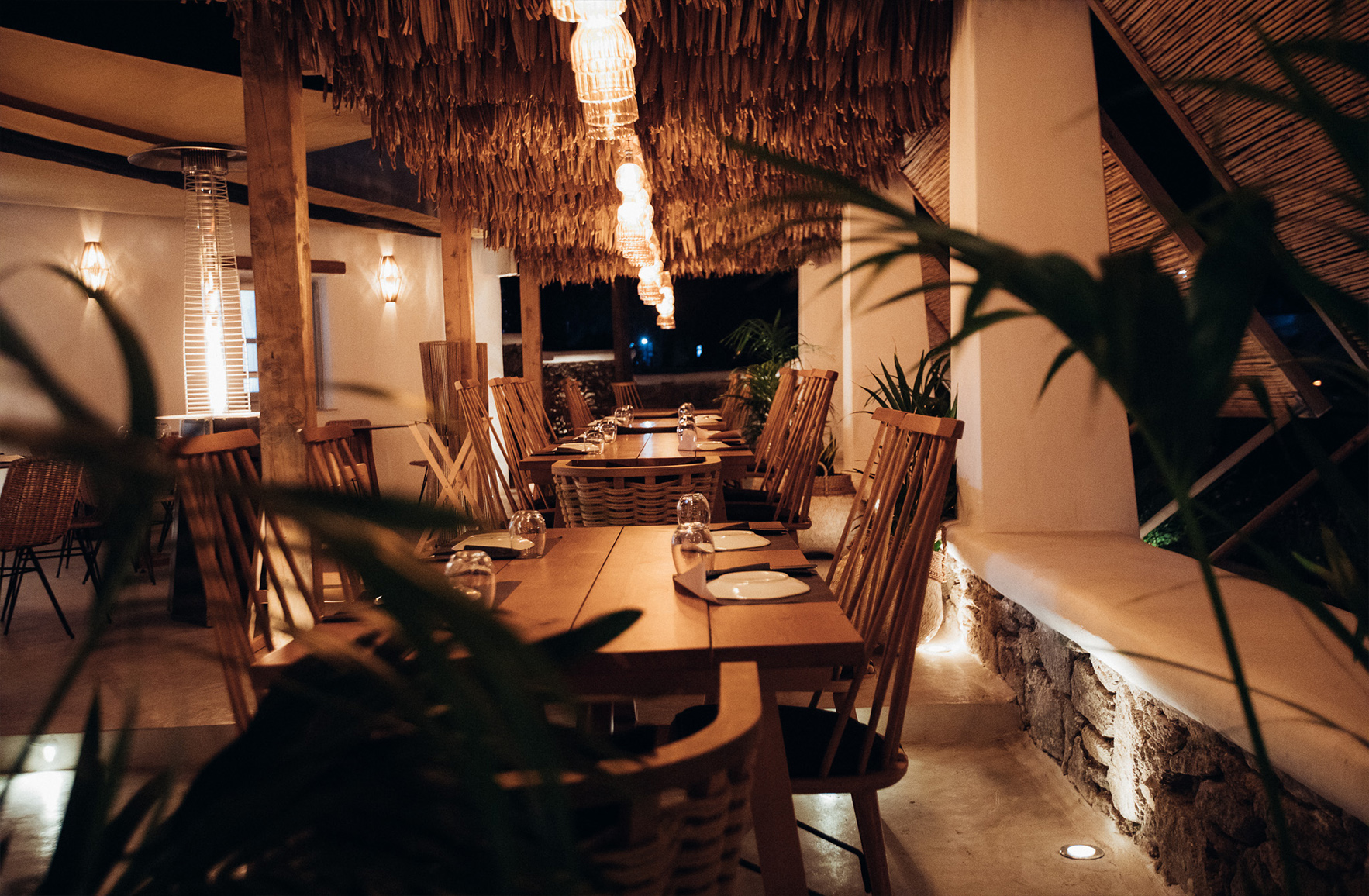 Atmospheric outdoor restaurant dining area beneath a timber pergola covered by makuti in Mykonos
