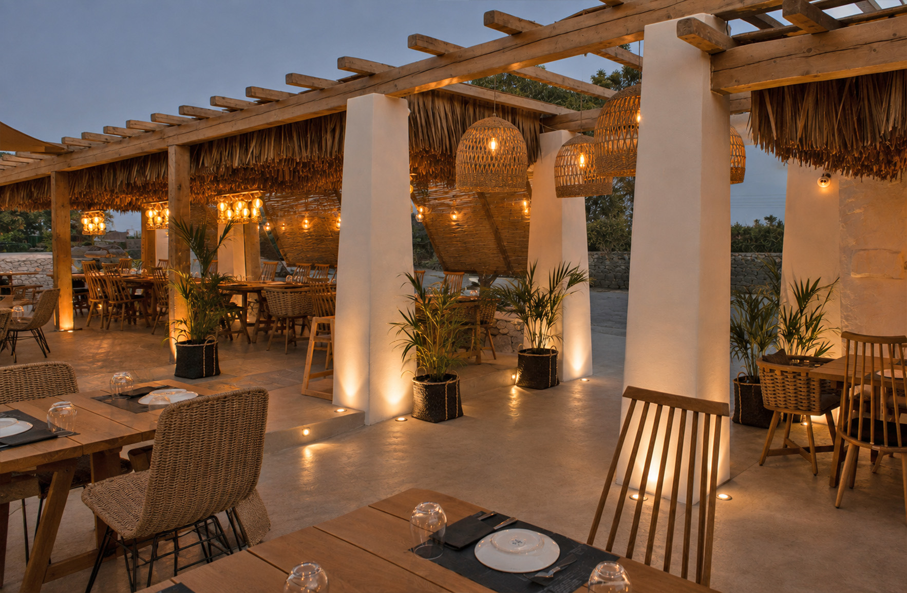 Outdoor restaurant terrace in Mykonos at sunset with warm ambient lighting and contemporary Cycladic design