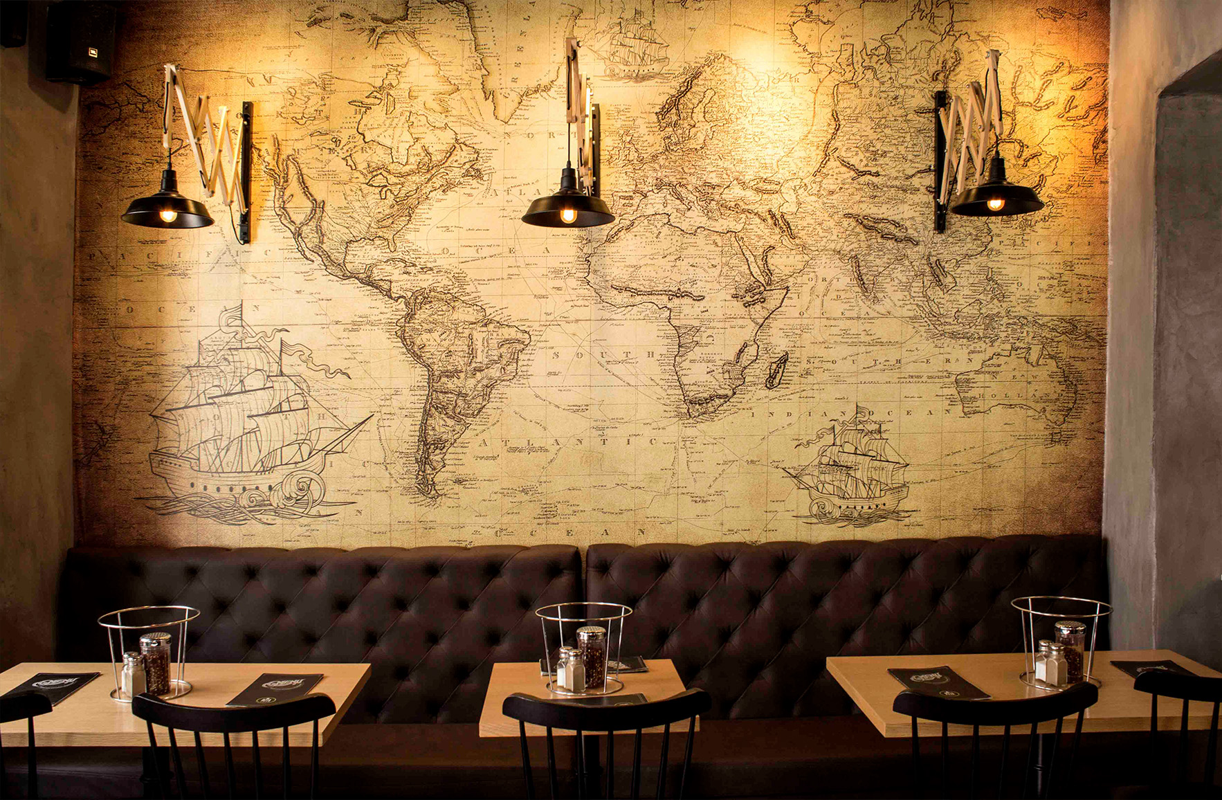 Interior of L’ Angolo Restaurant in Mykonos, featuring a vintage world map, sailing ships, wooden surfaces and warm lighting.