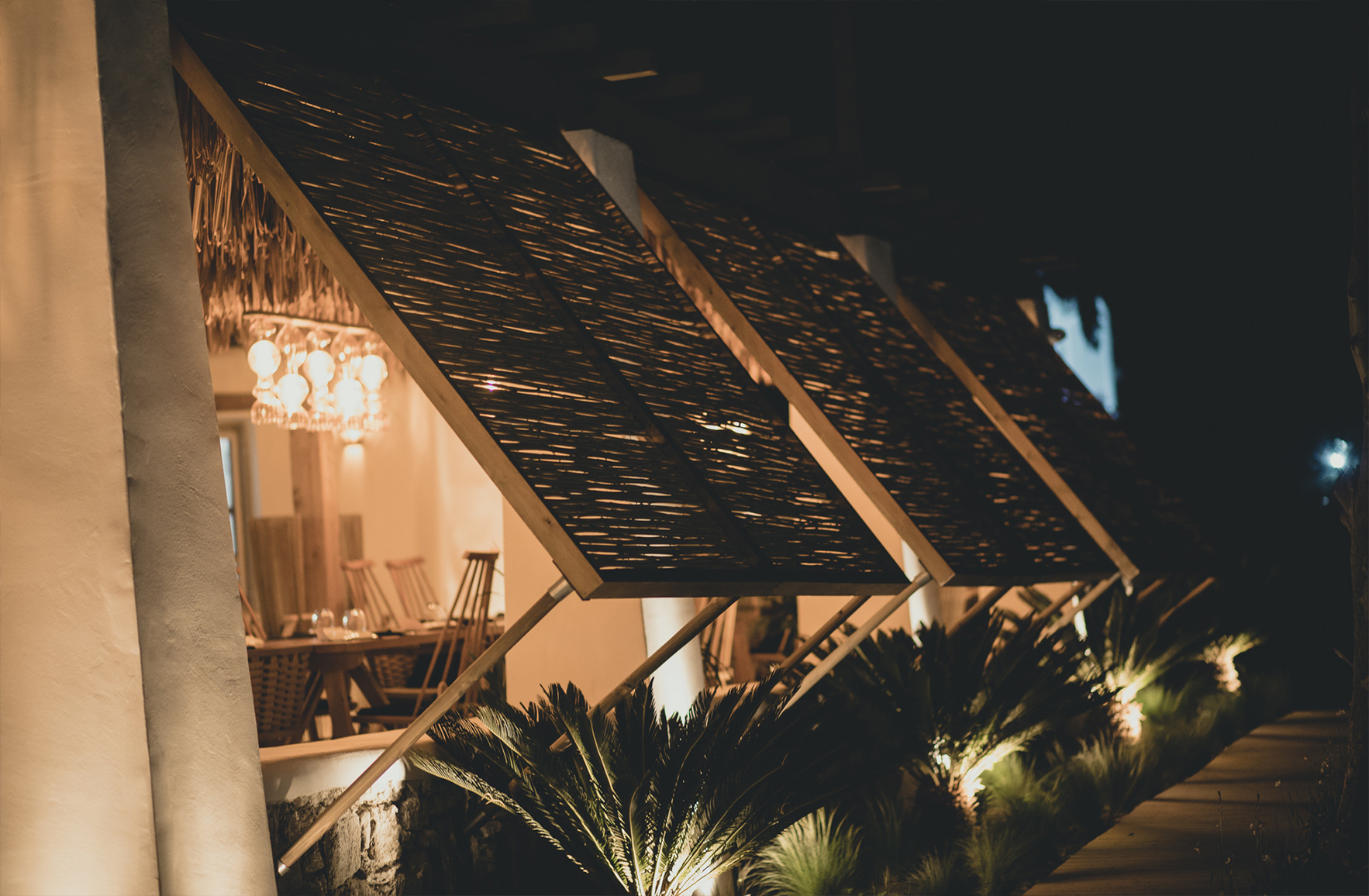 Outdoor restaurant in Mykonos at twilight with timber and reed window screens coveredby warm ambient lighting