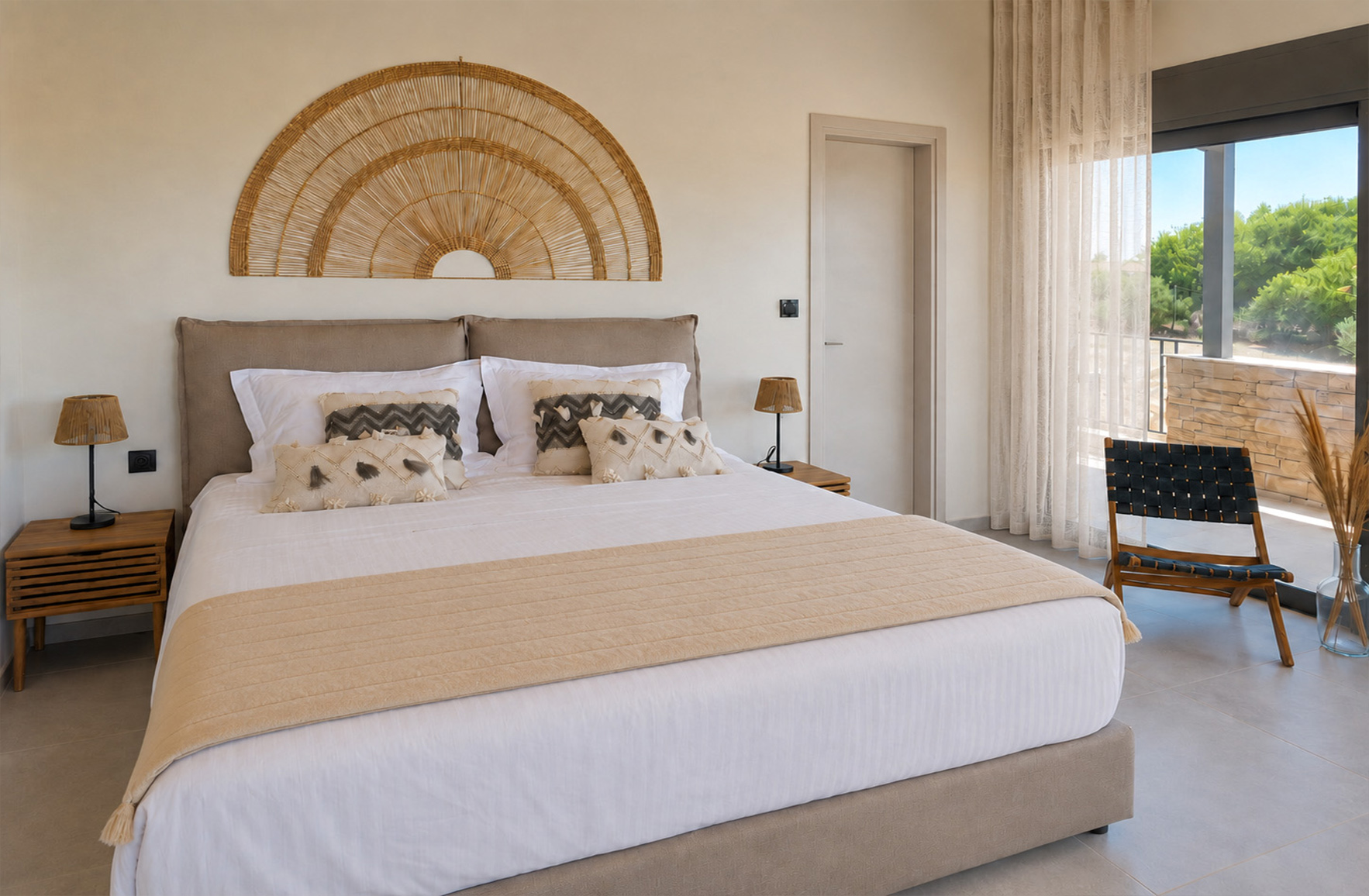 Neutral bedroom with woven wall décor, natural textiles and sheer curtains opening onto a balcony in a Skaloma seaside home.