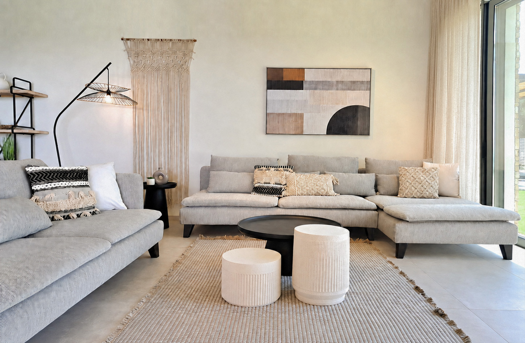 Seaside living room with light grey sofas, woven textiles, macramé wall hanging and sheer linen curtains in a Skaloma holiday home.